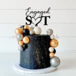 Engaged initial cake topper with love heart in black acrylic. ! tier black cake with gold accents.